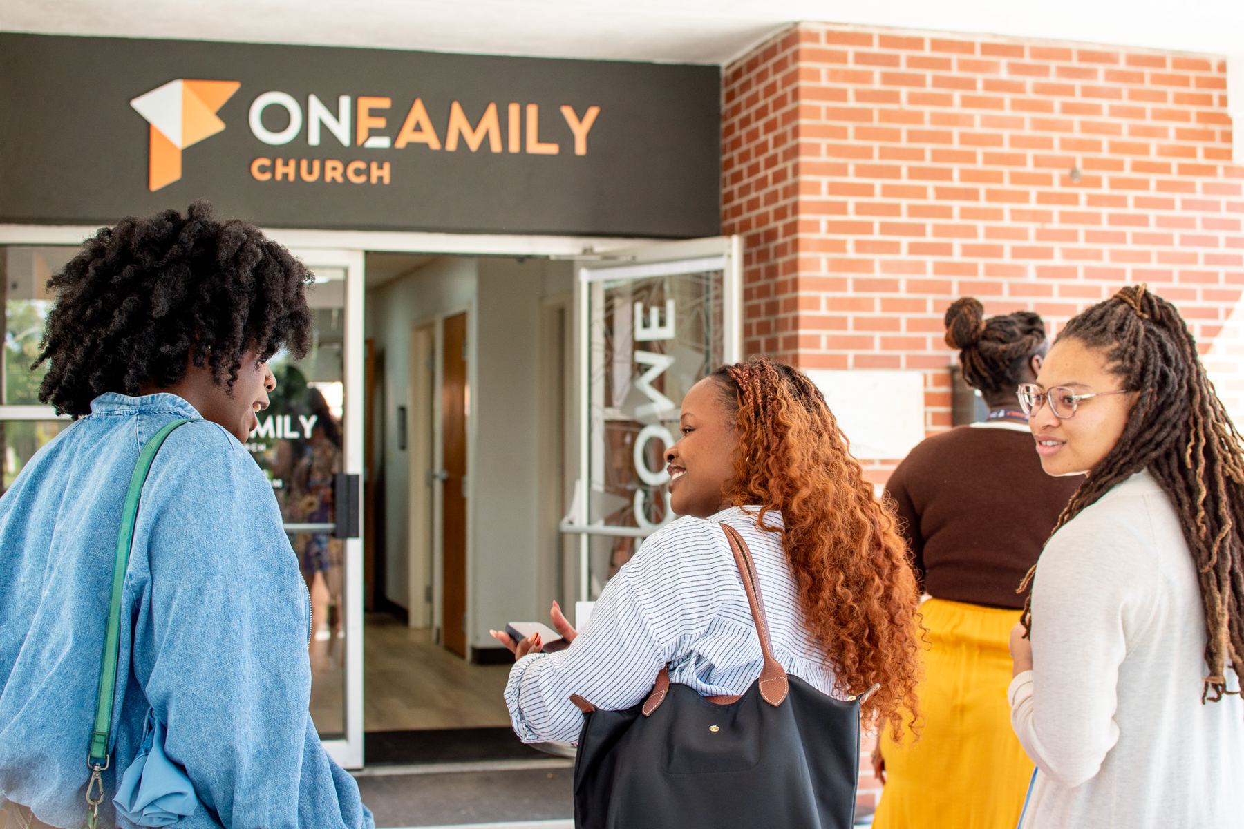 Friends walking into One Family Church under the church sign on a Sunday morning