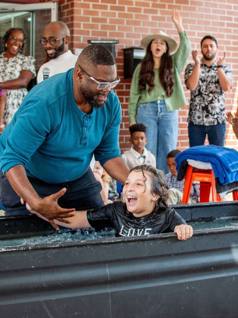 A pastor baptizing a smiling young woman as the church cheers
