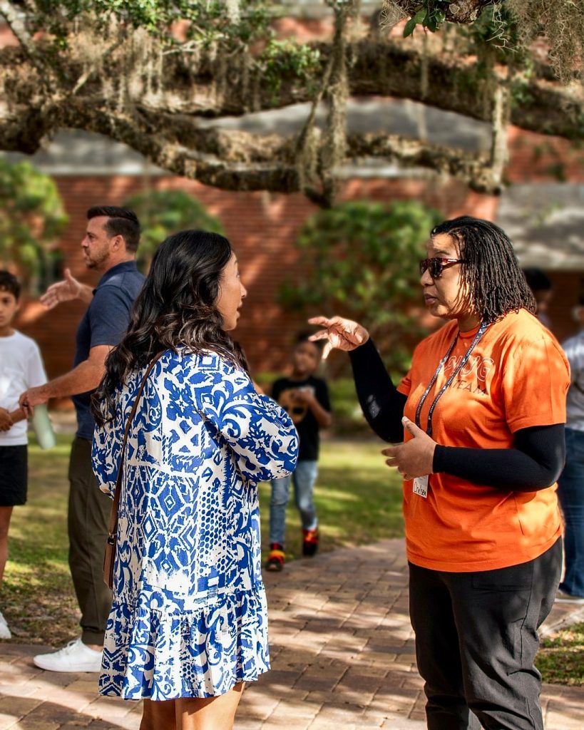 A volunteer in an orange shirt greeting a guest in the church courtyard