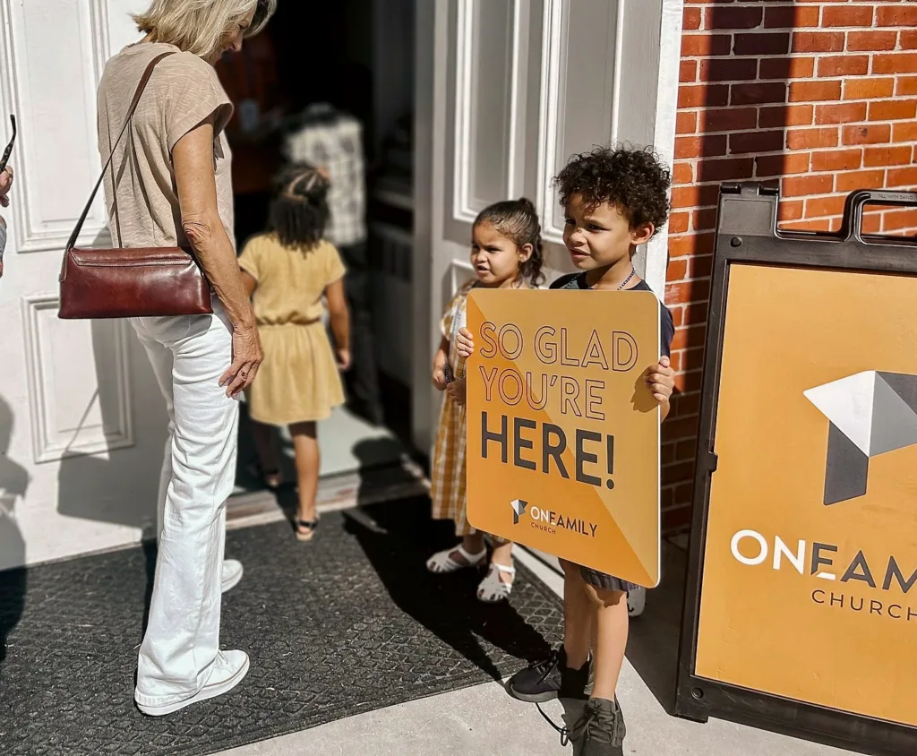 Kids holding a So glad you're here sign at the church's front door